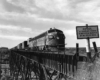 Streamlined diesel locomotives lead freight train on high steel bridge.