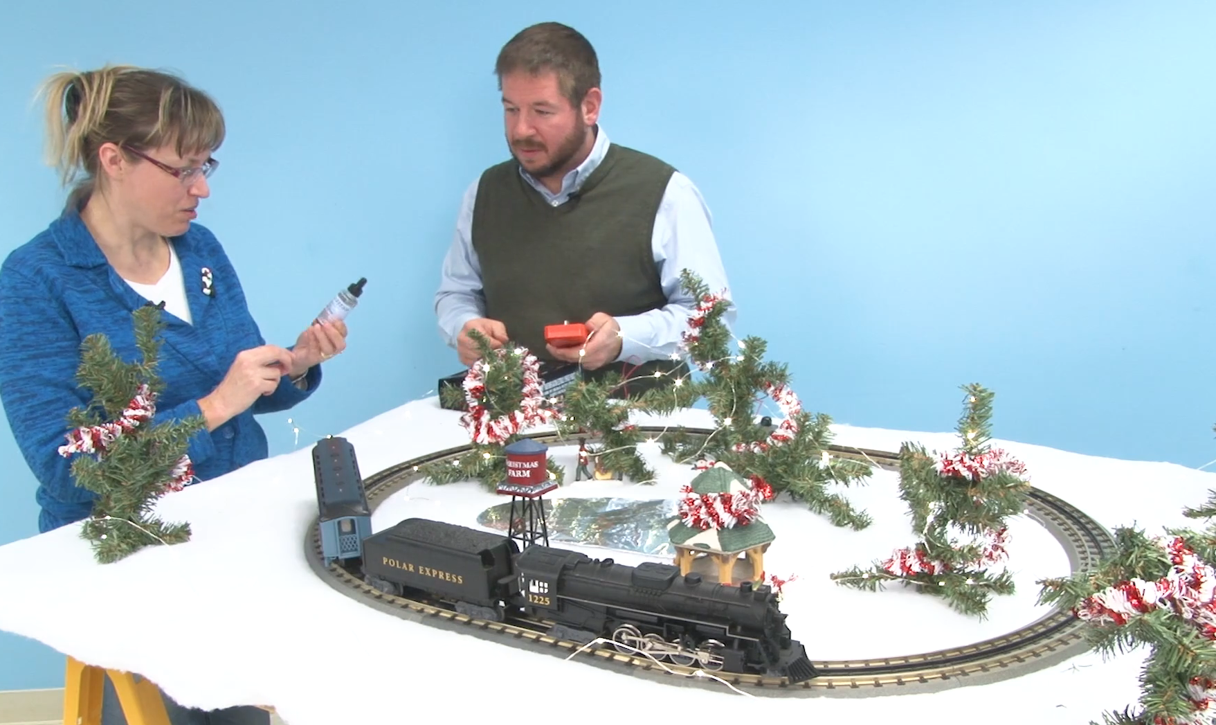 Two people with a budget Christmas train layout in a workshop.