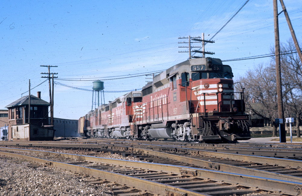 Four red-and-gray diesels pull a freight through an interlocking on a clear winter day