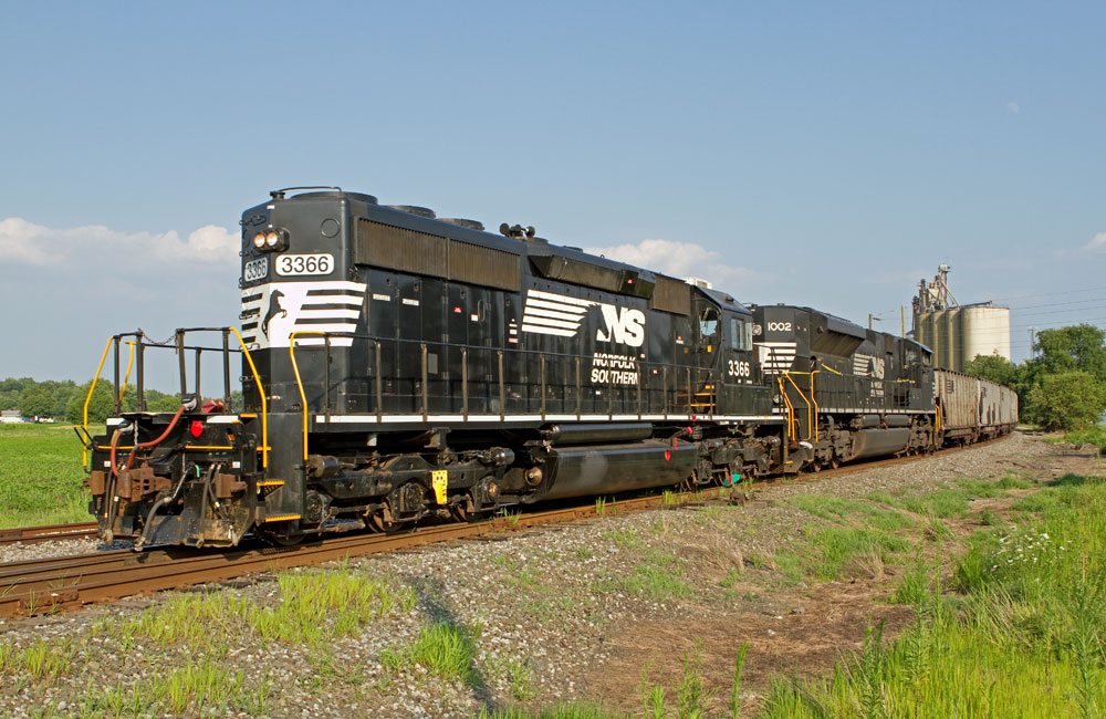 Two black Norfolk Southern diesel locomotives pull a string of empty hopper cars