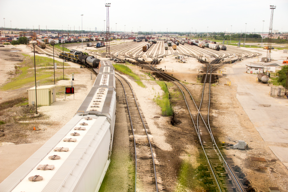 View of large classification yard with train pushing cars upgrade in foreground.