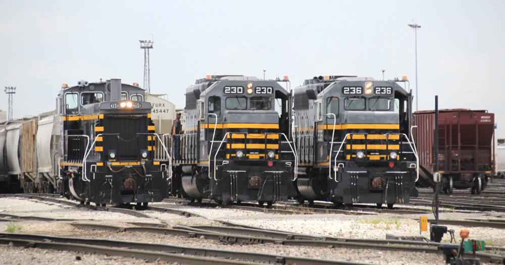 Three gray, black, and yellow locomotives lined up on yard tracks.