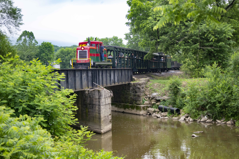 Red and green centercab diesel leads train across bridge