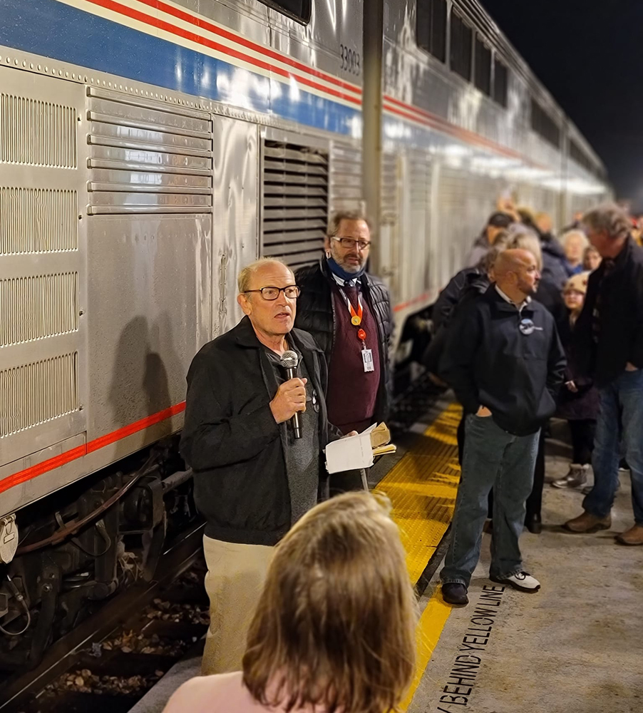 Man speaking on station platform with train in background