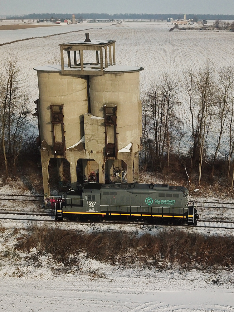 Gray locomotive passes grain elevator