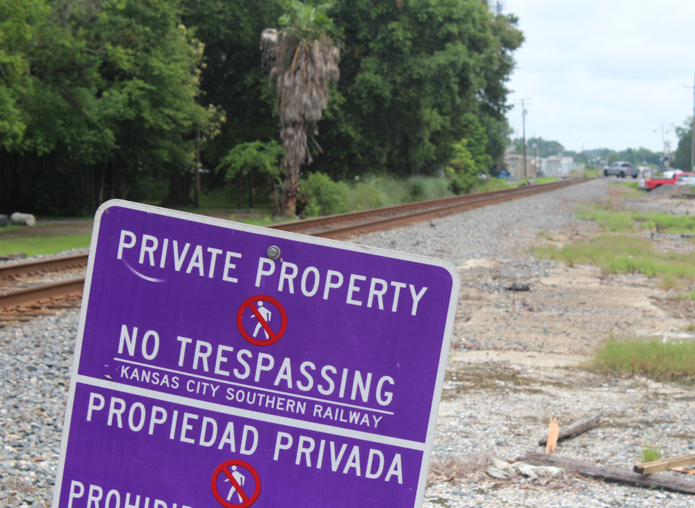 Vacant lot next to railroad track with "no trespassing" sign in foreground.