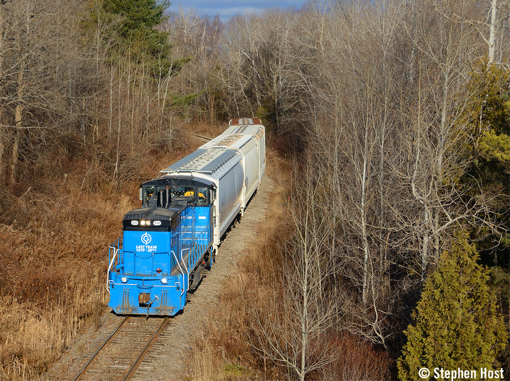 Blue and black locomotive leads freight cars along line surrounded by trees