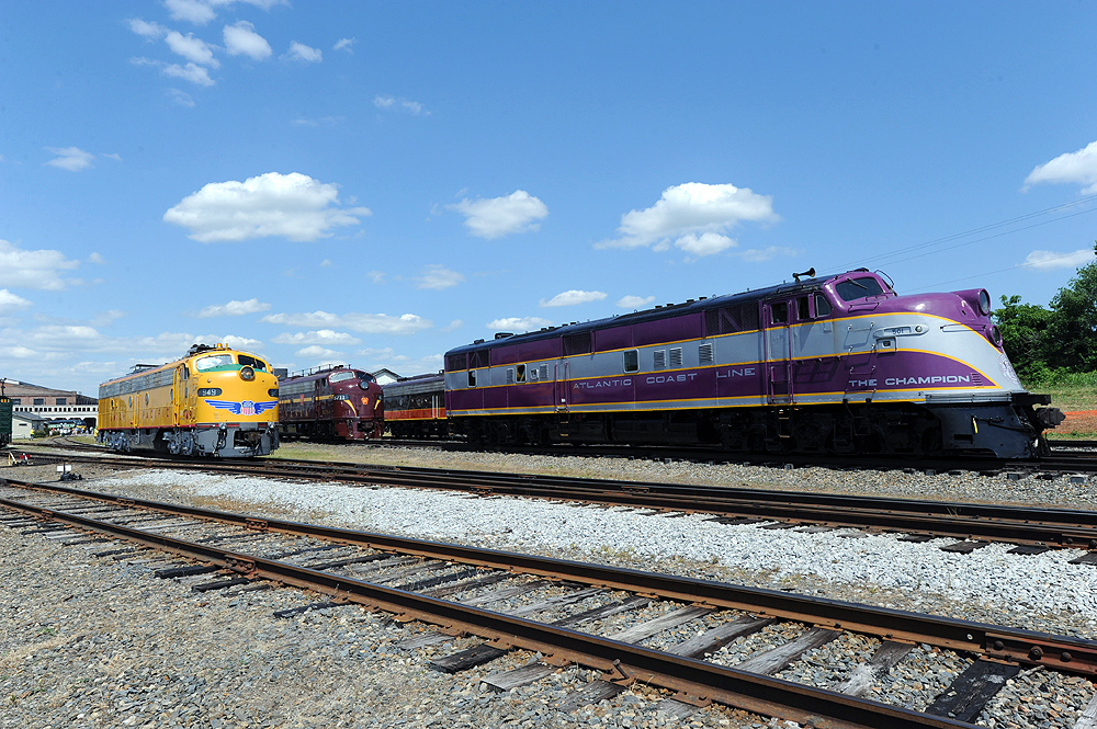 A purple and silver locomotive appears on rail yard tracks.