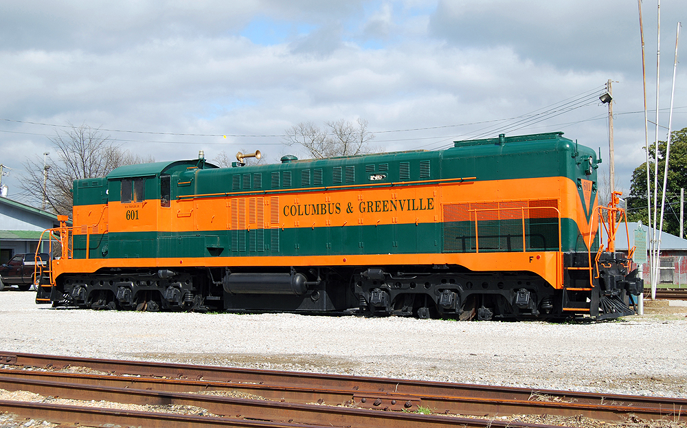 A green and orange-painted locomotive sits near a rail yard.