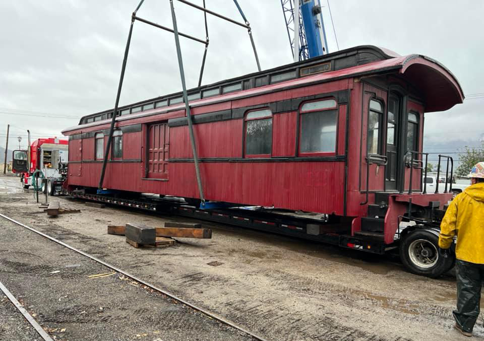 Red wooden passenger car is loaded on to truck trailer