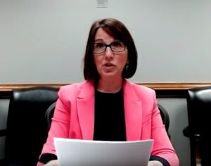 Woman in pink coat and black blouse reading from papers