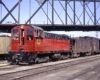 Red and black diesel locomotive with caboose and train under bridge