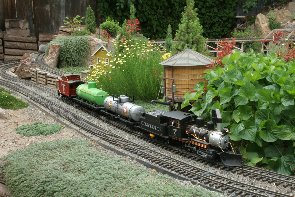Model steam engine passes a water tower on a garden railway