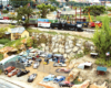 Steam locomotive passes near an auto junk yard on a garden railway