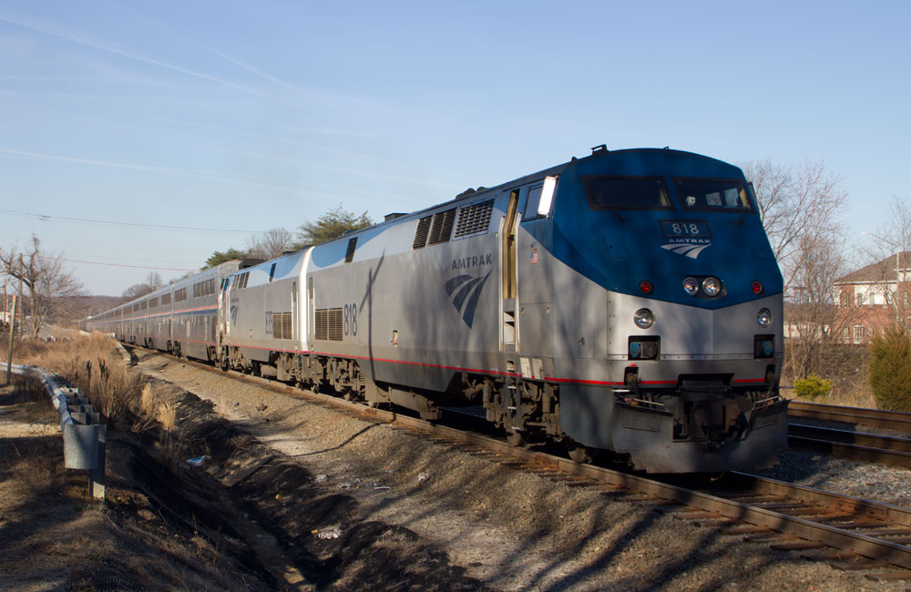 A silver and dark blue General Electric diesel locomotive leads a train of silver bi-level passenger cars