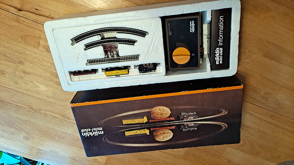 Brown boxtop with Styrofoam insert. Locomotive and two cars, sections of track in tray next to brown power pack.