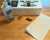 70 percent isopropyl alcohol, plastic-compatible oil in needle-nosed bottle, Bright Boy track cleaner bar, paper towel in front of Styrofoam trainset box insert.