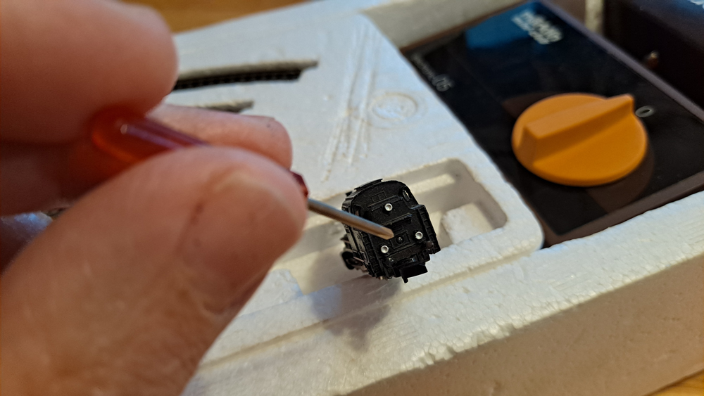 Rear of locomotive with small Phillips screwdriver pointing to pin holding locomotive body to frame.
