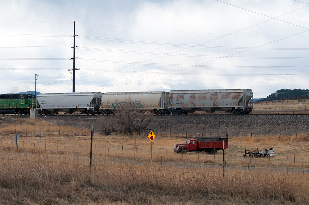 Three covered hoppers and an old pick-up truck in a field.