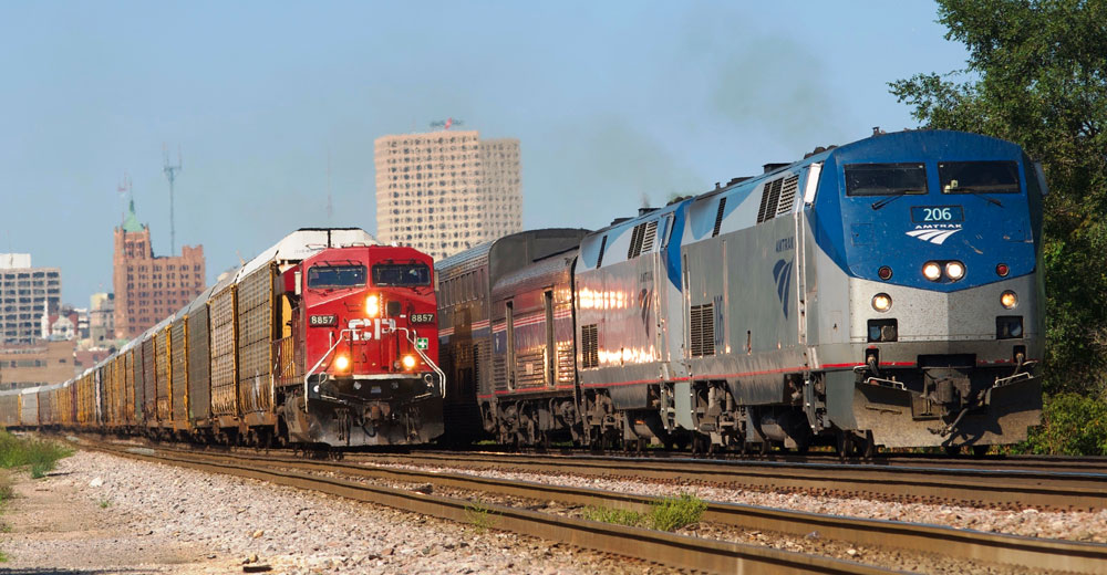 gray and blue passenger train passes next to red locomotive pulling freight train