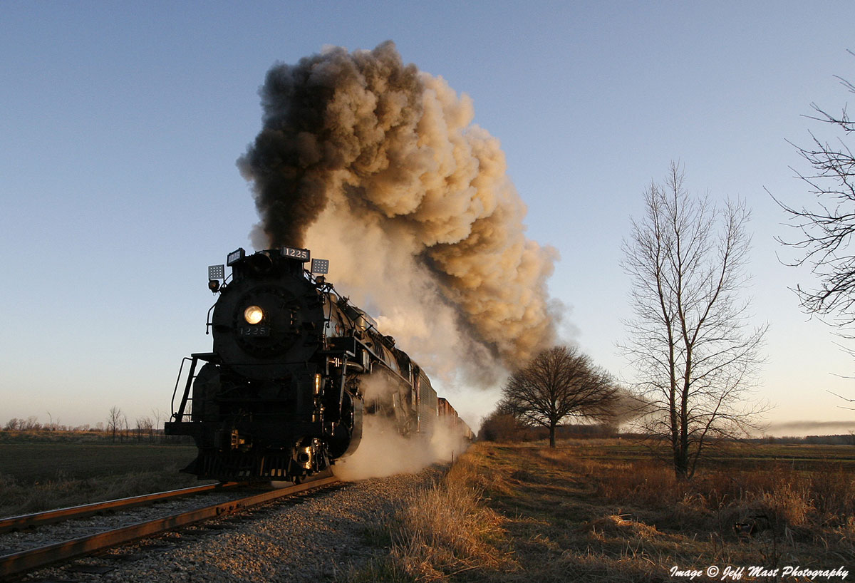 black steam locomotive with large smoke plume on a clear blue sky day