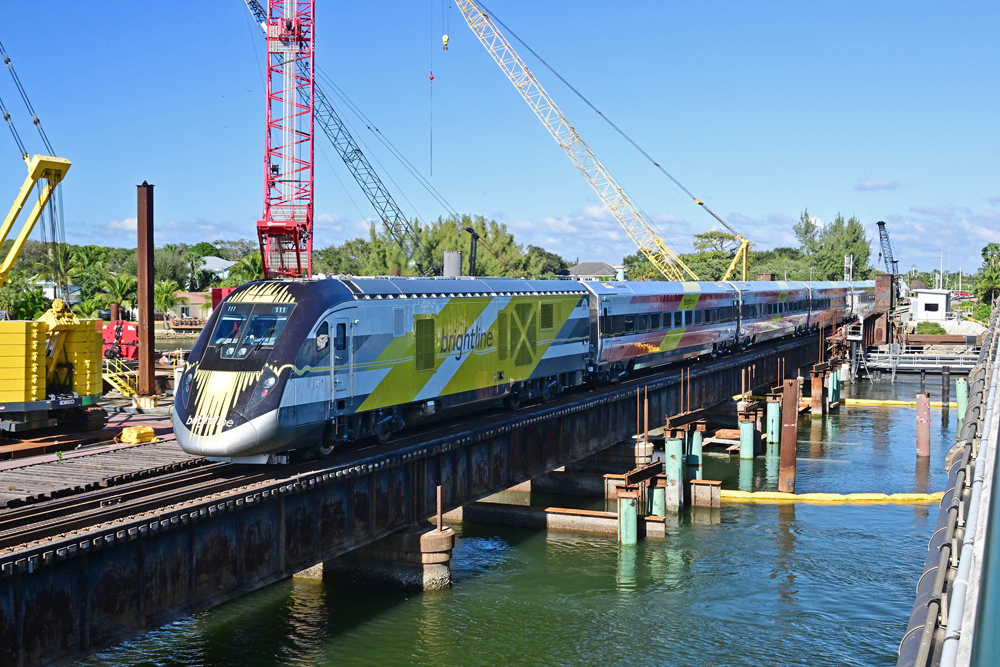 Passenger train crossing bridge surrounded by construction equipment