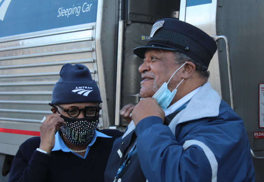 Man and woman Amtrak employees, wearing masks, standing next to sleeping car