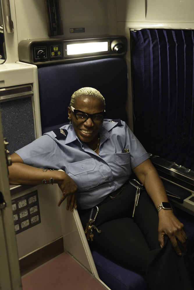 Woman with glasses and short hair, wearing Amtrak attendant uniform, in sleeping car