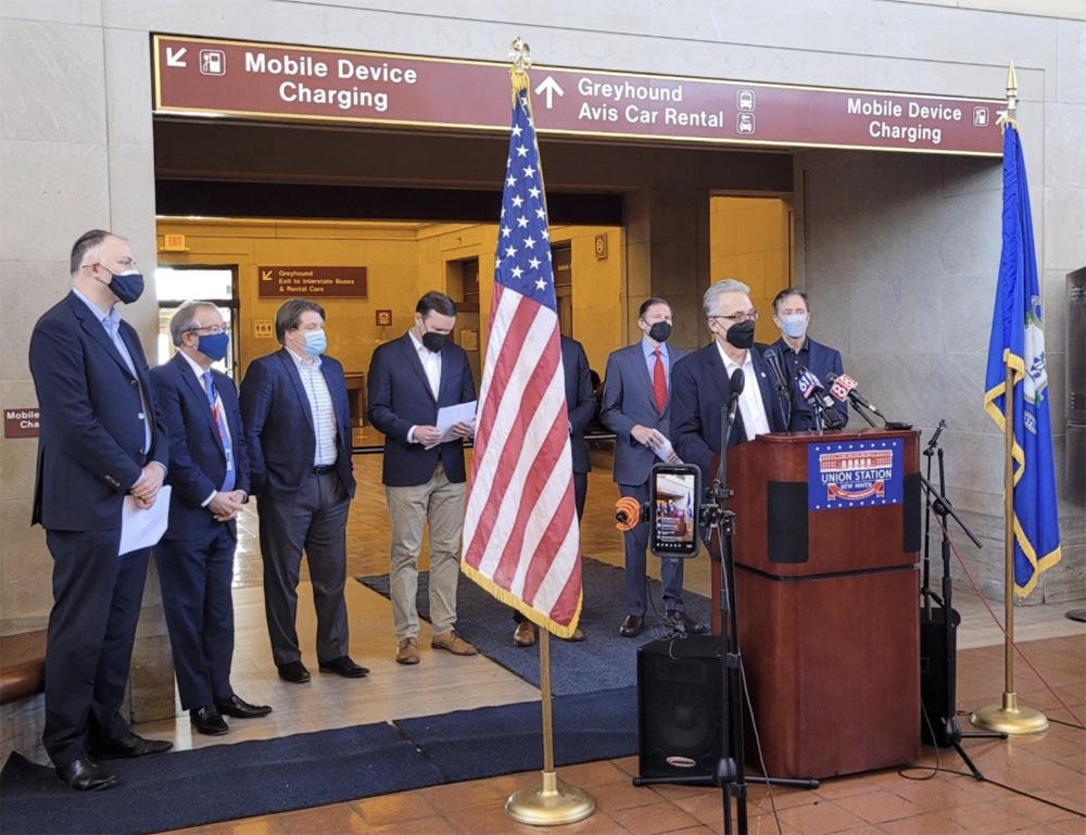 Man speaking at podium with others standing behind