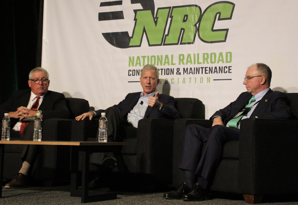 Three men seated on stage, talking