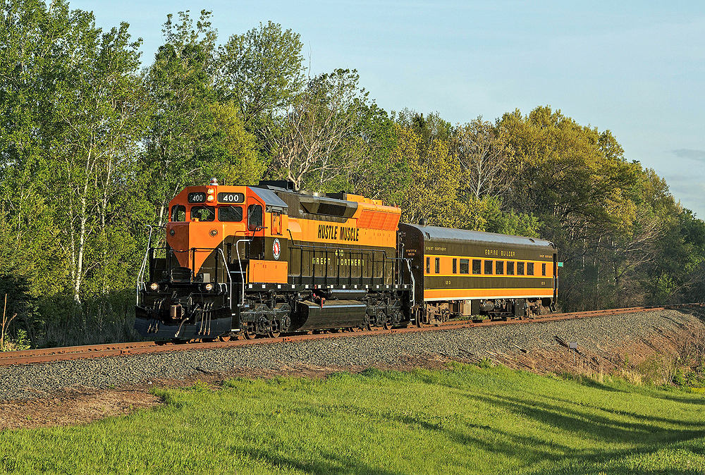 Orange locomotive and coach in a country scene.