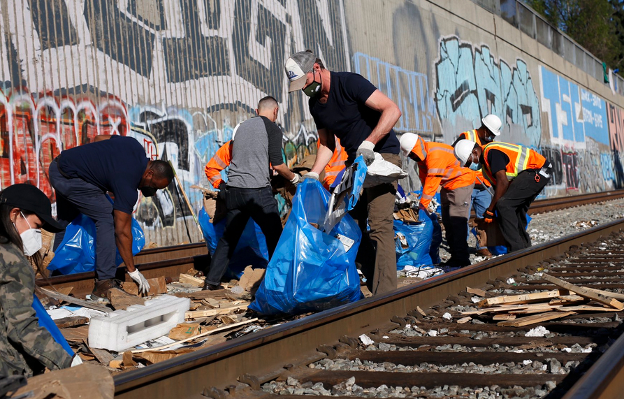 People with plastic bags picking up trash along railroad tracks