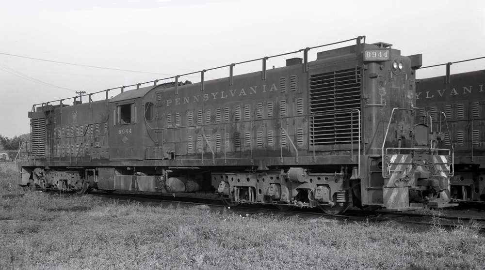 Black-and-white photo of long center-cab locomotive with three-axle trucks.