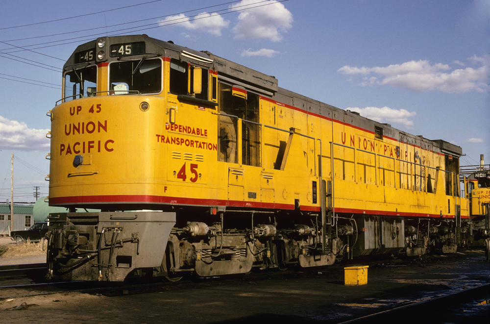 Yellow, red, and gray locomotive with short nose and eight axles.