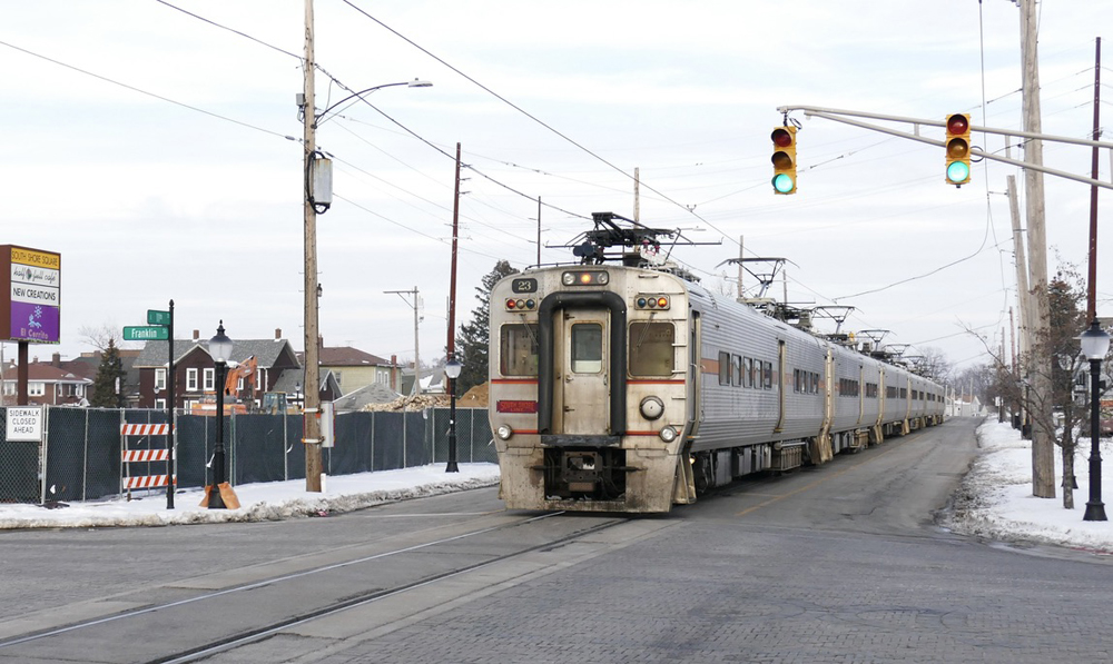 Commuter train running down middle of the street past fenced-off lot