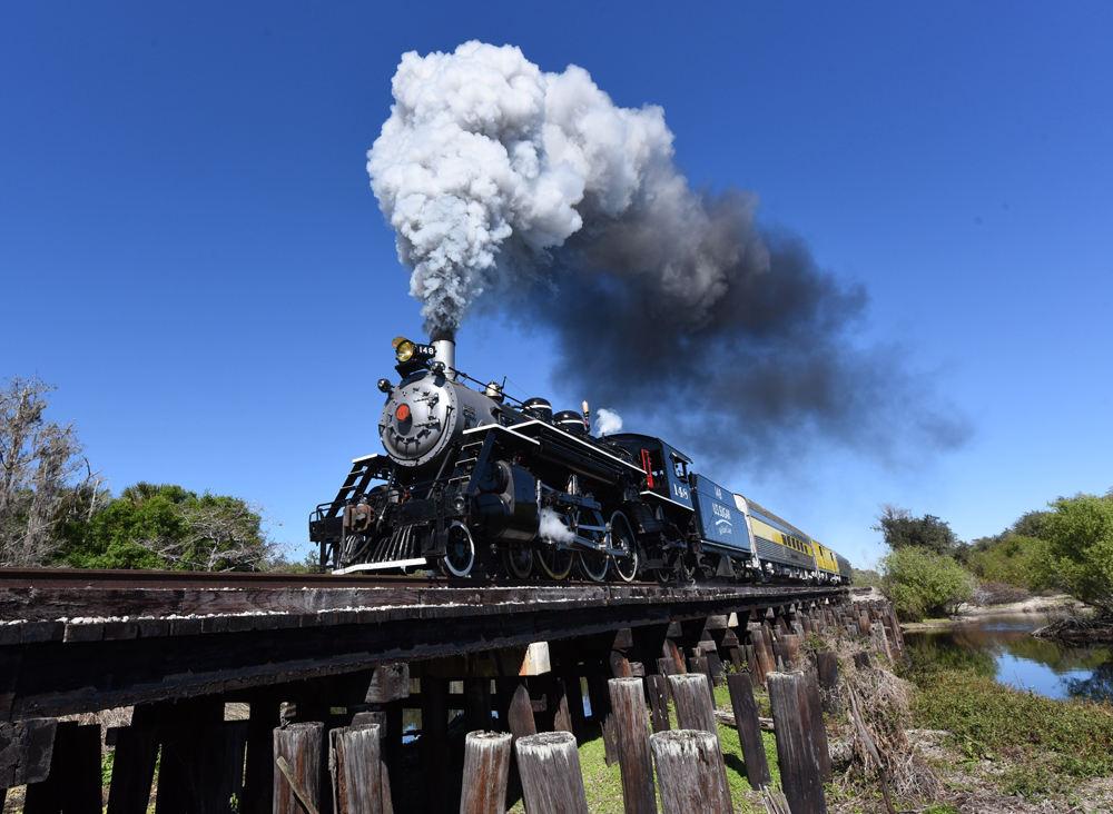 Train with steam locomotive crosses wooden bridge