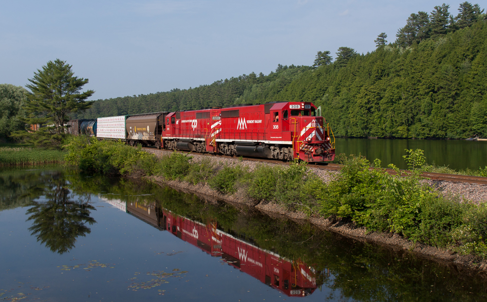 Red locomotives lead train along river