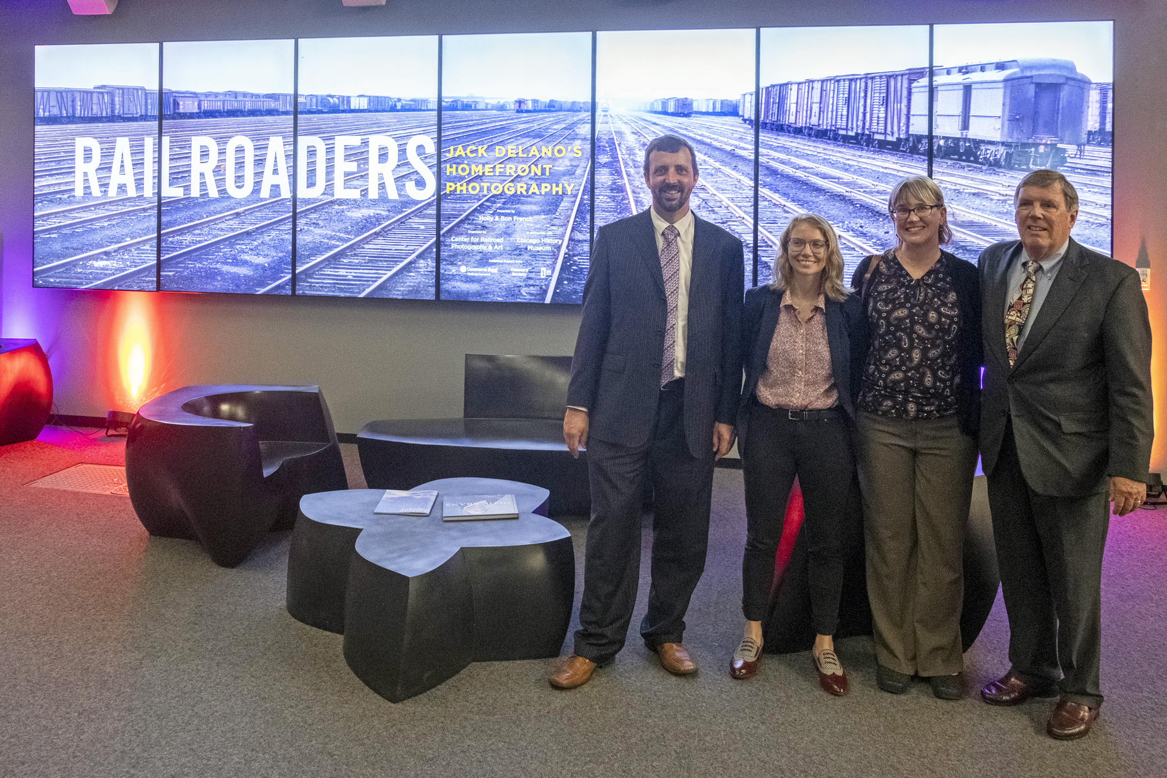 Four people standing in front of signage for "Railroaders" museum exhibit