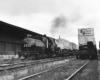 Southern Pacific freight trains: Steam locomotive pulls flat cars with trailers in yard alongside warehouse