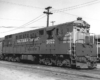 Diesel locomotives with high walkways rest in yard with passenger trains