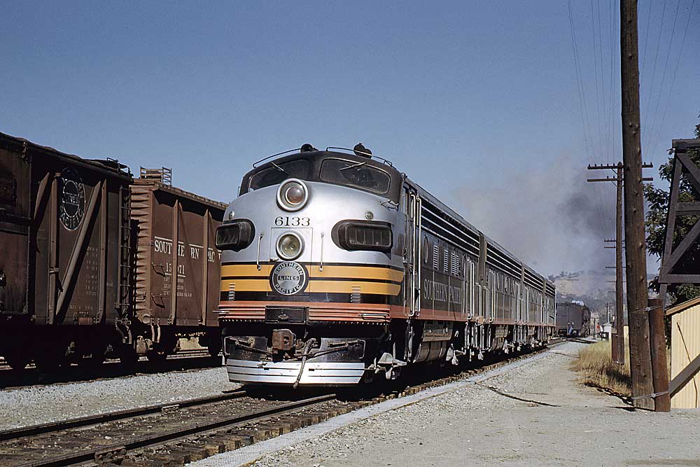 Black, silver and orange streamlined diesel locomotives beside wooden boxcars