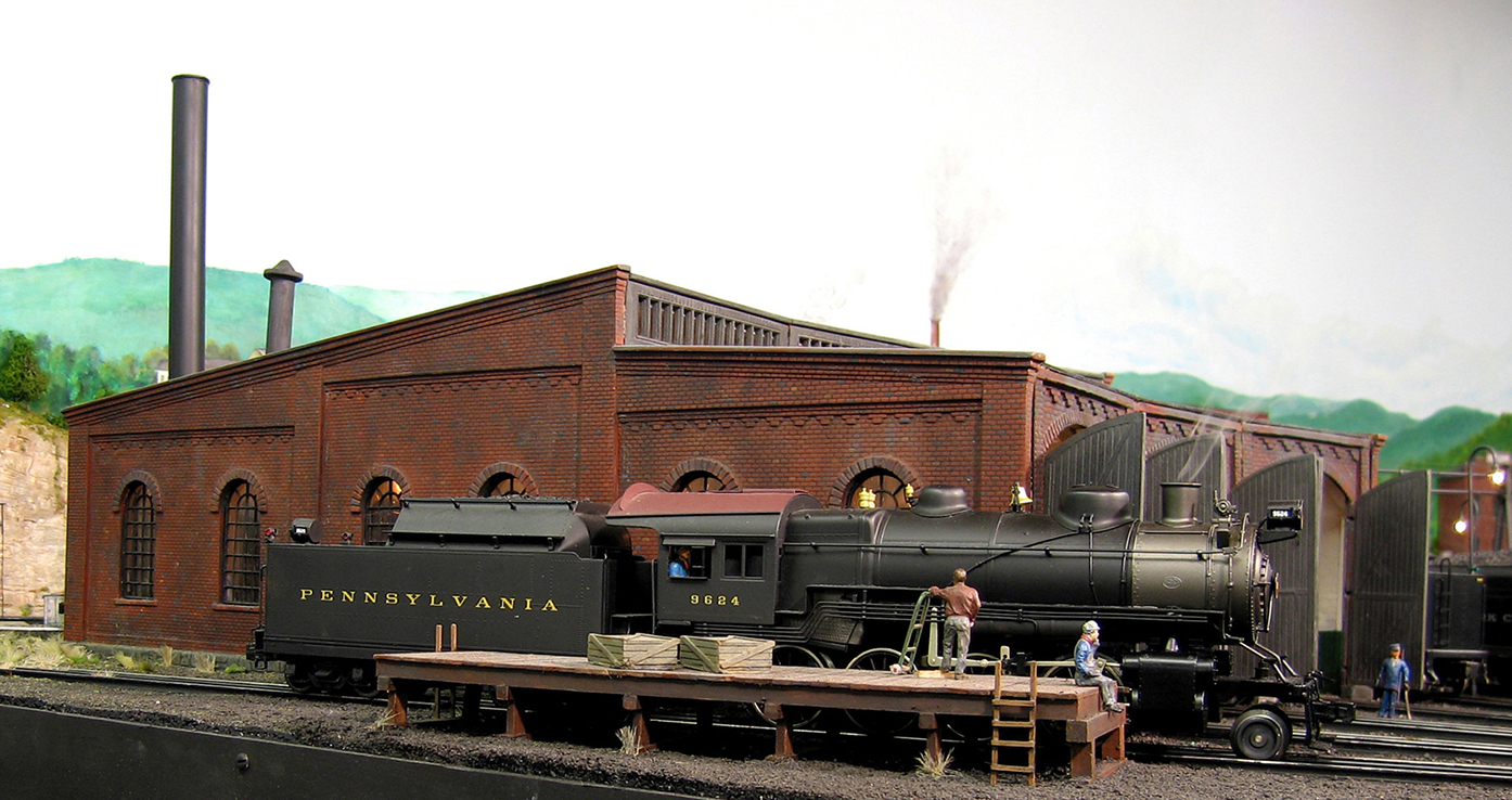 Steam engine in front of roundhouse.