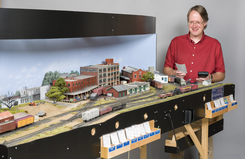 A man operates a train on a compact HO scale shelf layout