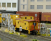 A gray-and-yellow diesel switcher shoves a matching-color caboose up to a servicing platform
