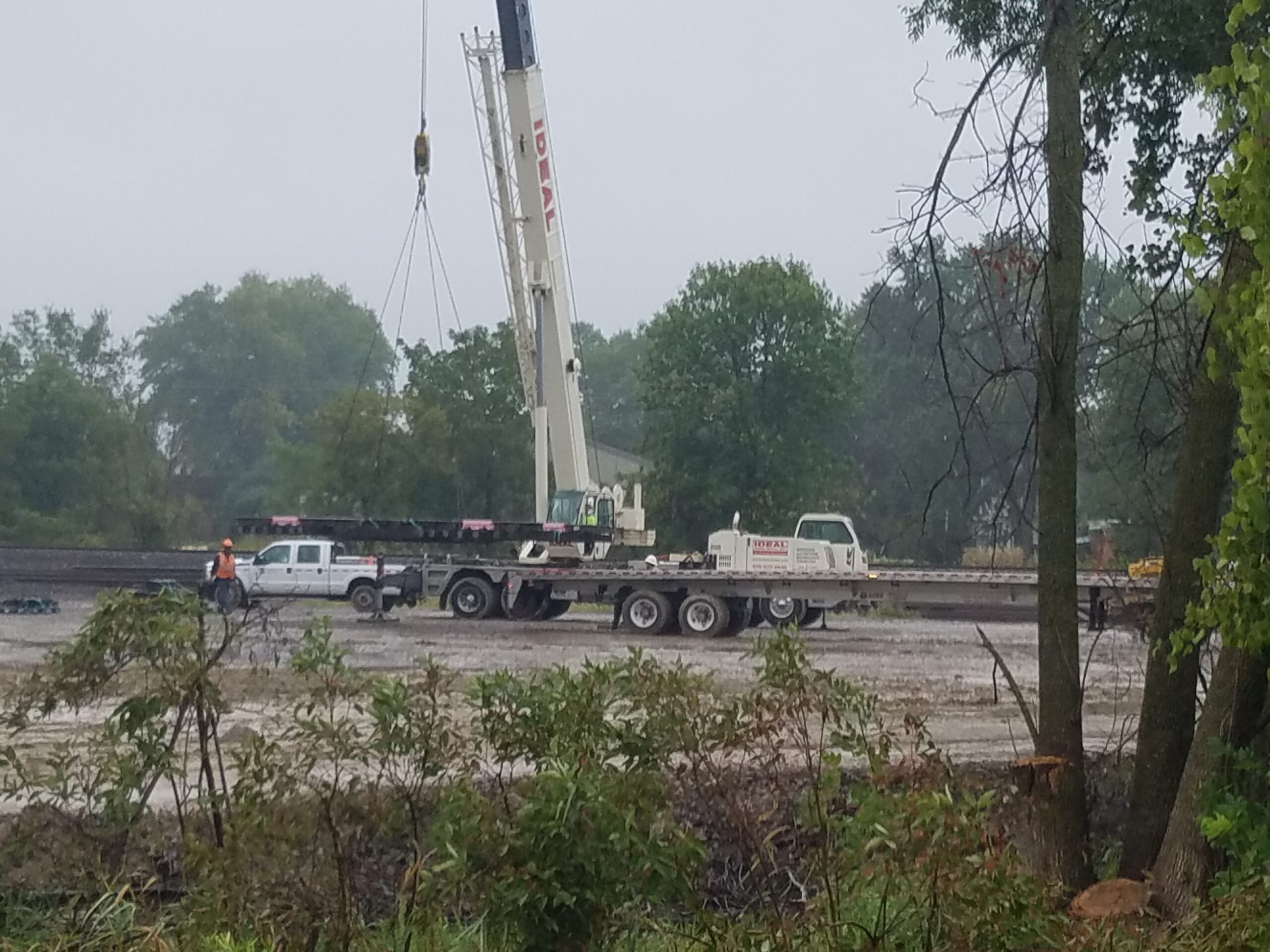 A white crane lifting a section of track from a flatbed trailer.