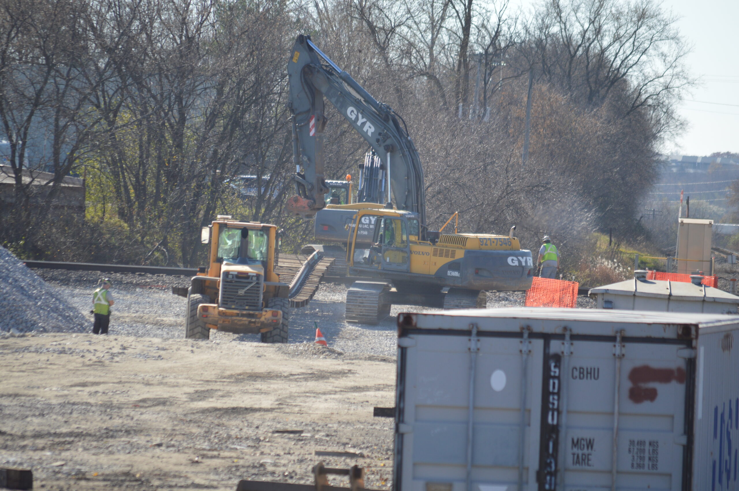 An excavator and a loader carry a section of panel track across the Canadian Pacific tracks.