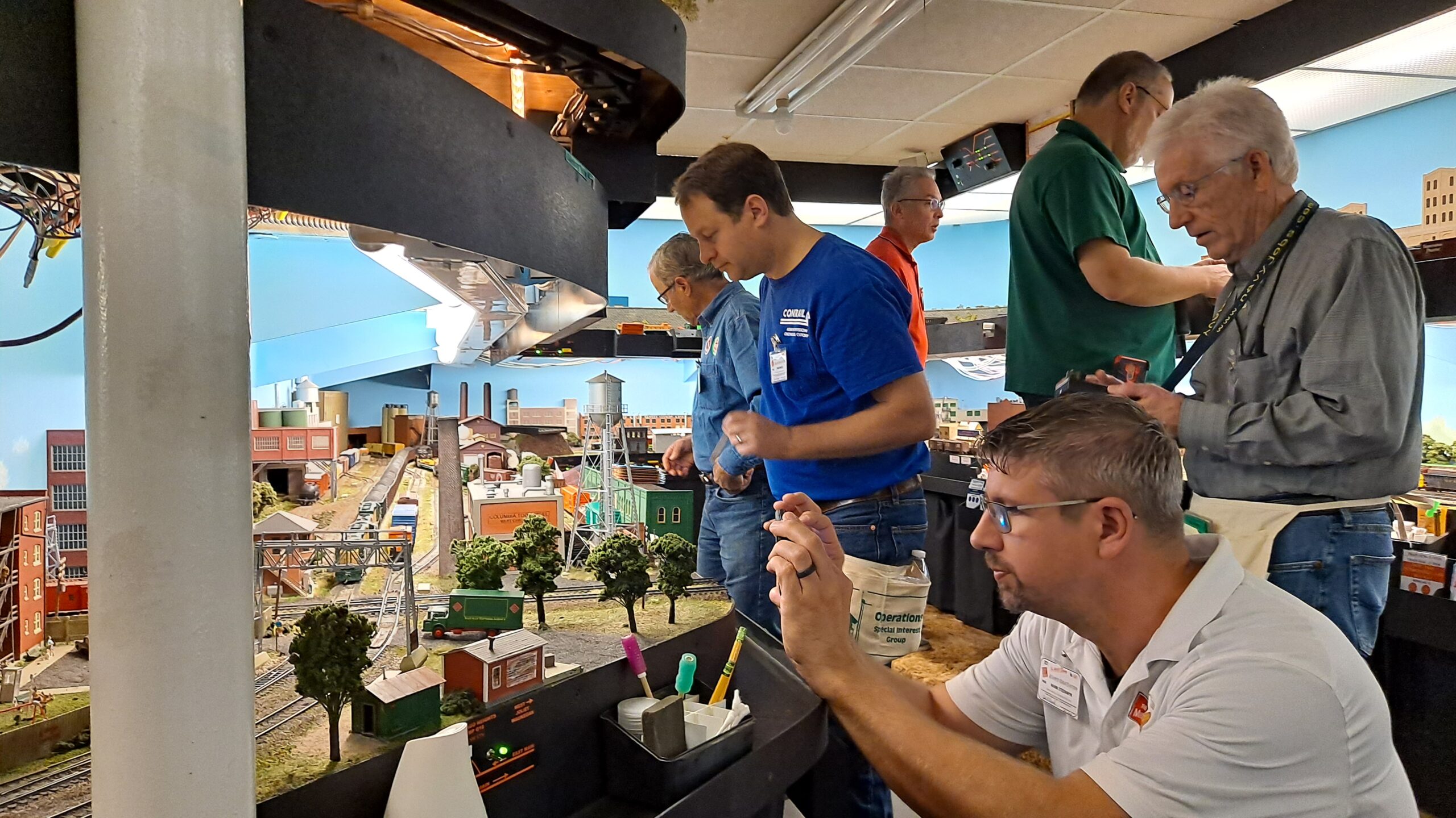 An operator kneels to photograph his train as five other operators run trains behind him on a double-deck layout.