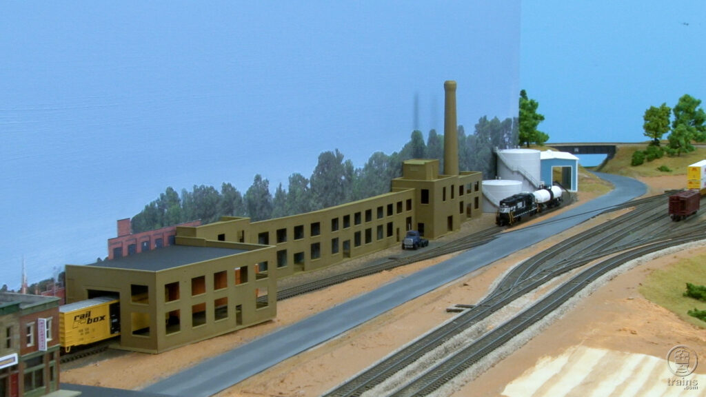 Kitbashed N scale buildings alongside a blue backdrop with tree line