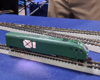 Green locomotive with lighted panel on side, sitting on gray and black plastic track.