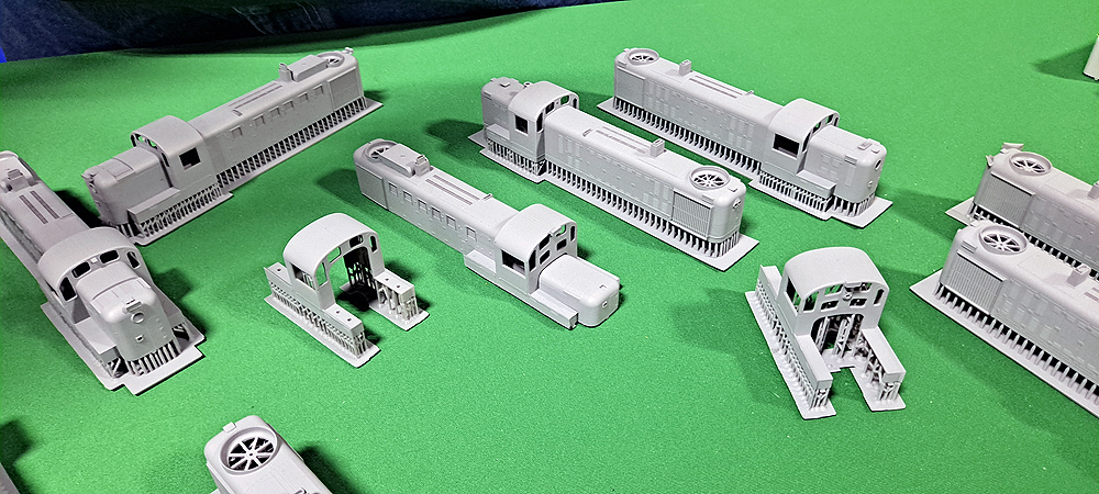 Gray 3-D printed plastic shells, some with their support structures still attached, are displayed on a green tablecloth.